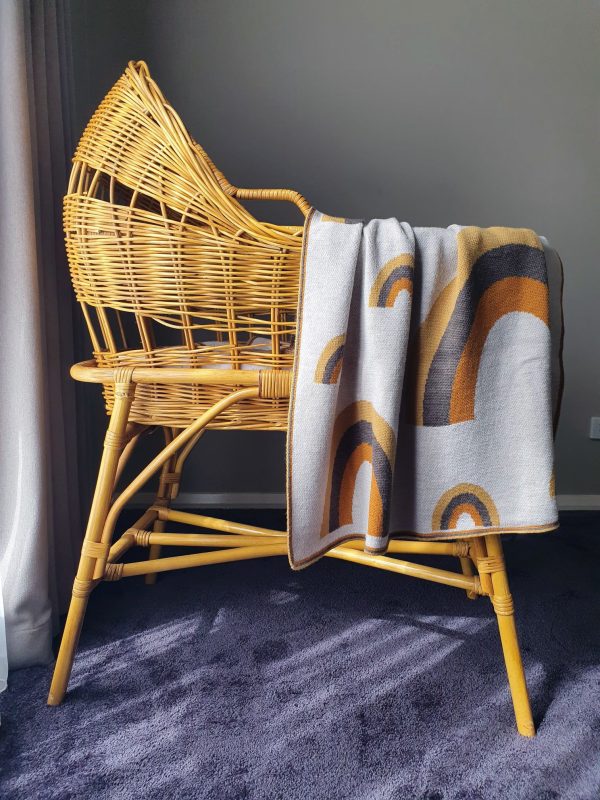 Merino wool Rainbow Baby Blanket in earthy shades, draped over a rattan bassinet