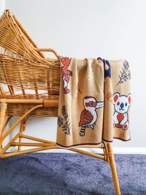 Australian Animals Blanket in Red Ochre draped over a rattan bassinet