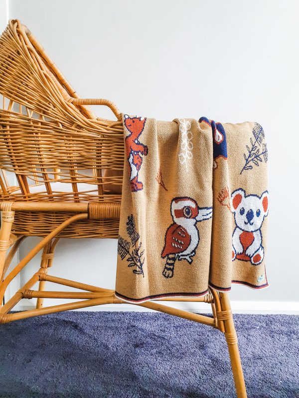 Australian Animals Blanket in Red Ochre draped over a rattan bassinet