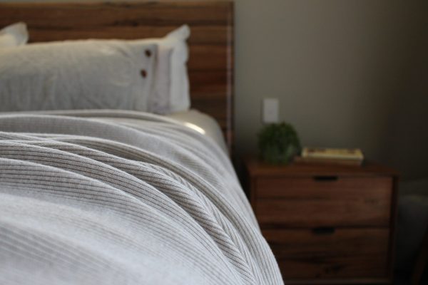 Australian Merino Wool Blanket - Bobbi in Cashew draped over a bed with a mini stripe design in light beige and white