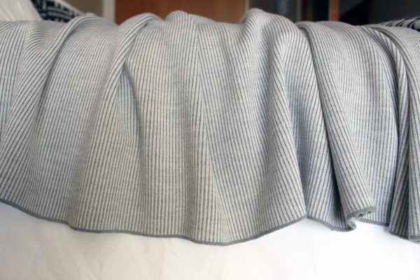 Silver Merino Wool Blanket in contrasting colours of grey and white, close-up, draped over the edge of a bed.