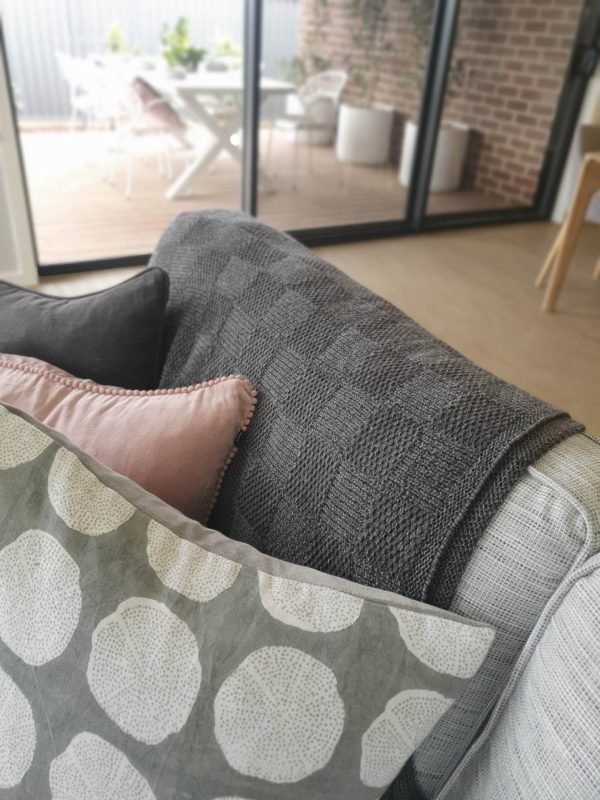 Pure Merino Wool Marley Blanket in Granite (mid grey), close-up draped over the back of a couch with stylish cushions. Front view for a chic perspective.