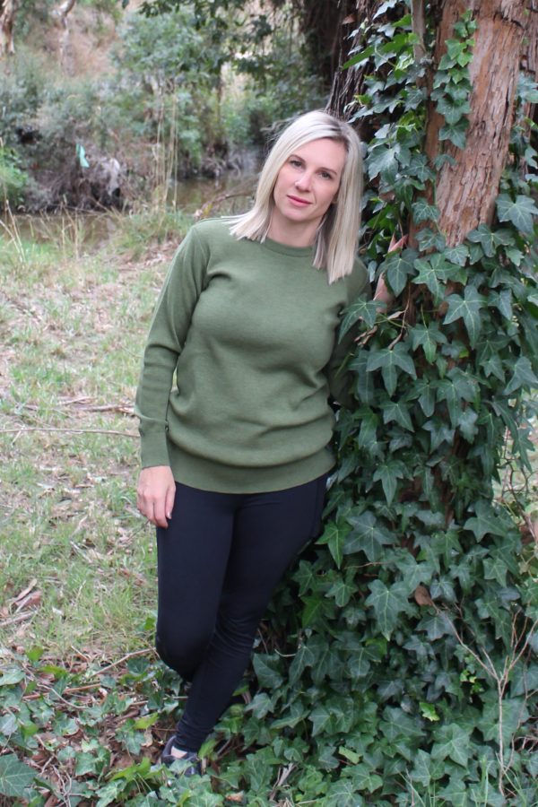 A lady leaning against a tree outside in the bush wearing a Ballarat Gold branded Australian made pure merino wool Sophie 1010 jumper in Olive green