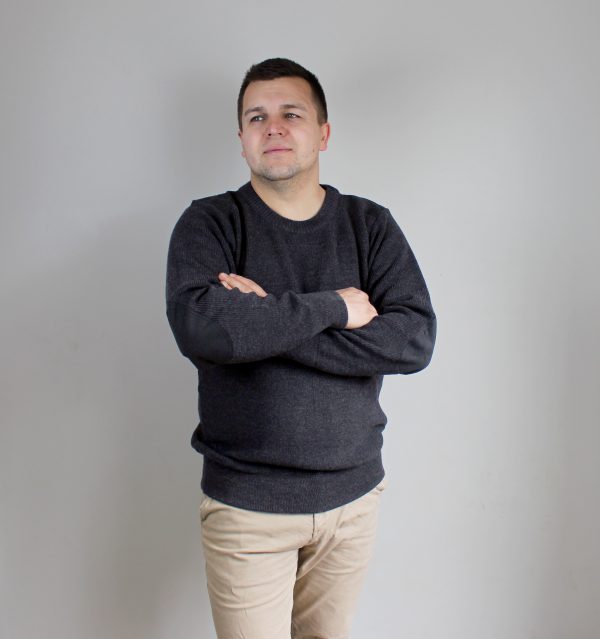 A man standing indoors wearing an Australian Made, pure merino woollen Ballarat Gold knitted jumper with suade patches.