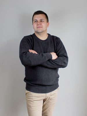 A man standing indoors wearing an Australian Made, pure merino woollen Ballarat Gold knitted jumper with suade patches.