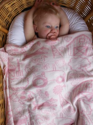 On The Farm Cot Blanket - a pale pink and white reversible design. Baby restfully laying in her bassinet with the folded blanket over her.