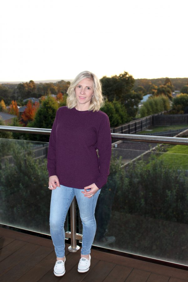 A lady wearing an Australian Made, Ballarat Gold merino wool moss crew jumper in Currant (purple)
