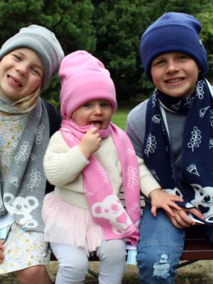 Three children sitting on a park bench wearing Branberry Australian Made, Merino wool Kids Koala Scarves and plain beanies