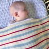 Blue, Red, and White Striped Garter Blanket made from a luxurious blend of cotton and wool. Close-up view showcasing the intricate stripes. Baby peacefully sleeping, wrapped in the cosy blanket.