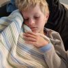 Striped Garter Blanket in Blue, Mint, and White, an image of a 10-year-old boy cuddling his blanket while sleeping