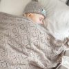 Branberry Heirloom Blanket in Cashew (beige), a baby sleeping soundly in a cot with the matching Pure Wool Frankie Beanie