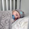 Branberry Heirloom Blanket in Cashew, a close-up view of a baby sleeping in a cot with the blanket and a matching Pure Wool Frankie Beanie.