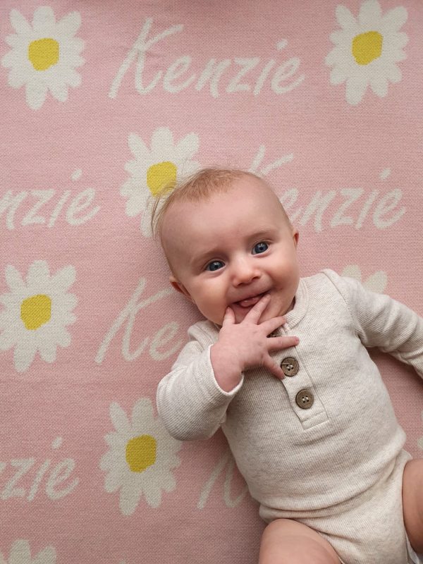 A baby laying on a Personalised Name Blanket with Daisy flowers in a Pastel Pink colour. Made from Pure Australian Merino Wool and Made in Australia.