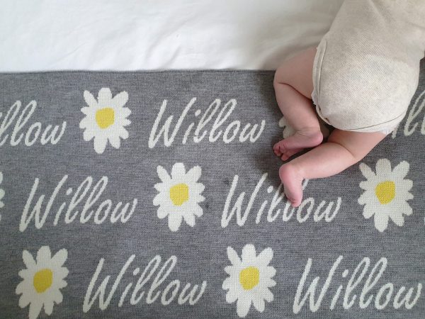 A baby laying on a Personalised Name Blanket with Daisy flowers in a Silver grey colour. Made from Pure Australian Merino Wool and Made in Australia.