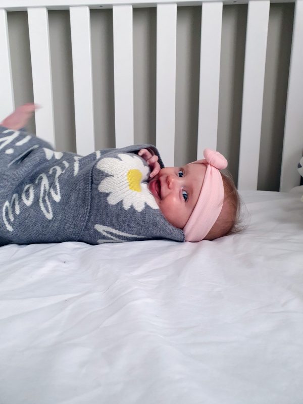 A baby swaddled with a Personalised Name Blanket with Daisy flowers in a Silver grey colour. Made from Pure Australian Merino Wool and Made in Australia.