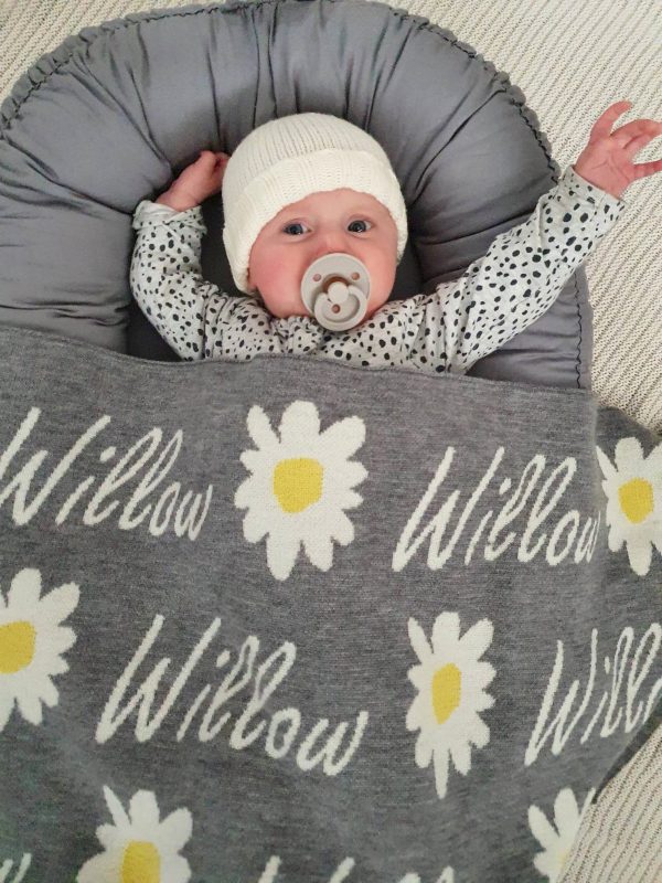 A baby tucked in bed with a Personalised Name Blanket with Daisy flowers in a Silver grey colour. Made from Pure Australian Merino Wool and Made in Australia.