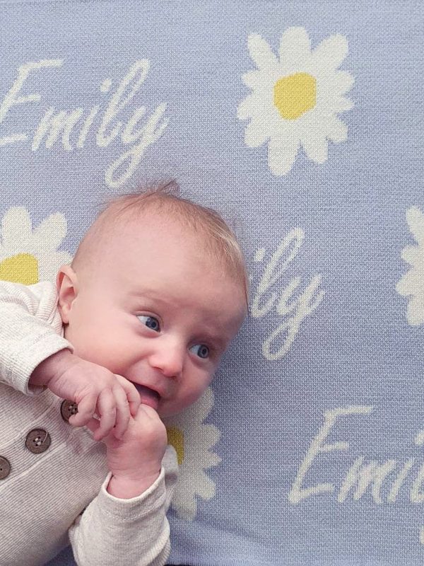 A baby laying on a Personalised Name Blanket with Daisy flowers in a Pastel Blue colour. Made from Pure Australian Merino Wool and Made in Australia.