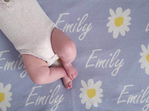 A baby laying on a Personalised Name Blanket with Daisy flowers in a Pastel Blue colour. Made from Pure Australian Merino Wool and Made in Australia.