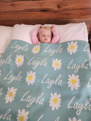 A baby sleeping under a Personalised Name Blanket with Daisy flowers in a Seafoam green colour. Made from Pure Australian Merino Wool and Made in Australia.