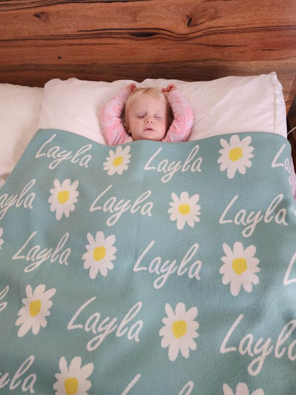 A baby sleeping under a Personalised Name Blanket with Daisy flowers in a Seafoam green colour. Made from Pure Australian Merino Wool and Made in Australia.