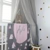 A Personalised Name Blanket with sporadic triangles with a big circle in the centre with a custom name, in a grey, pink and white colour combo draped over a cot. Made from Pure Australian Merino Wool and Made in Australia.