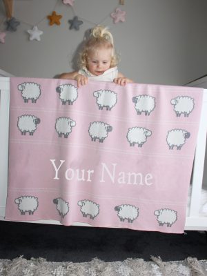 A toddler leaning on her Personalised Pure Australian Merino wool Sheep blanket in Pink, that's placed over a cot
