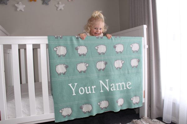 A toddler leaning on her Personalised Pure Australian Merino wool Sheep blanket in Seafoam Green, that's placed over a cot