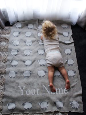 A toddler laying on top of a Personalised Pure Australian Merino wool Sheep blanket in light Grey.