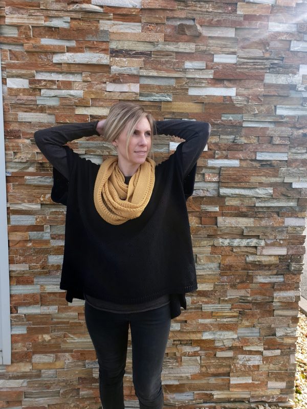 A woman wearing the Harlow Poncho in black, paired with a mustard vintage lace scarf, basking in sunlight.