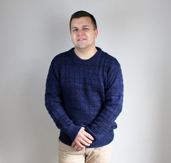 A man wearing Deep Ocean, Michael Bricks designed jumper, looking at the camera with his hands crossed in front of him.