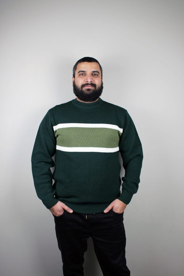 A man standing and wearing the Forest Noah Striped Jumper, a moss stitch knitted pullover in forest green with olive green and white stripes across the chest.